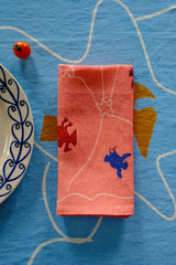 Folded pink fabric with colorful designs on a blue textured surface.