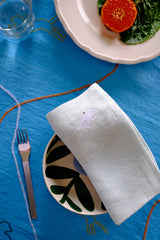 Dessert setting with a white plate, dessert, and a napkin on a blue tablecloth.