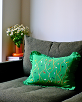 Green embroidered pillow on an olive green sofa with a vase of flowers in the background