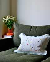 Decorative pillow with playful embroidery on a green sofa next to a vase with flowers