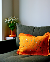 Orange pillow with embroidery on a green sofa next to a vase with flowers