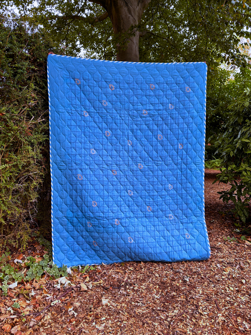 Blue quilted cover on a mattress outdoors with trees in the background