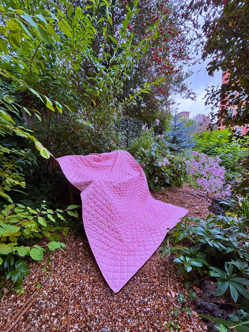 Pink quilt draped over a bench in a garden setting