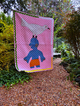 Pink quilt with a blue character and bird design in a garden setting