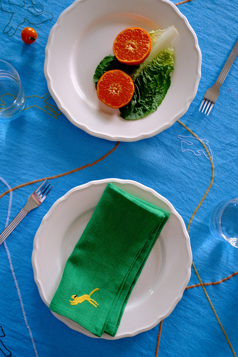 Two white plates with green napkins and orange slices on a blue tablecloth.