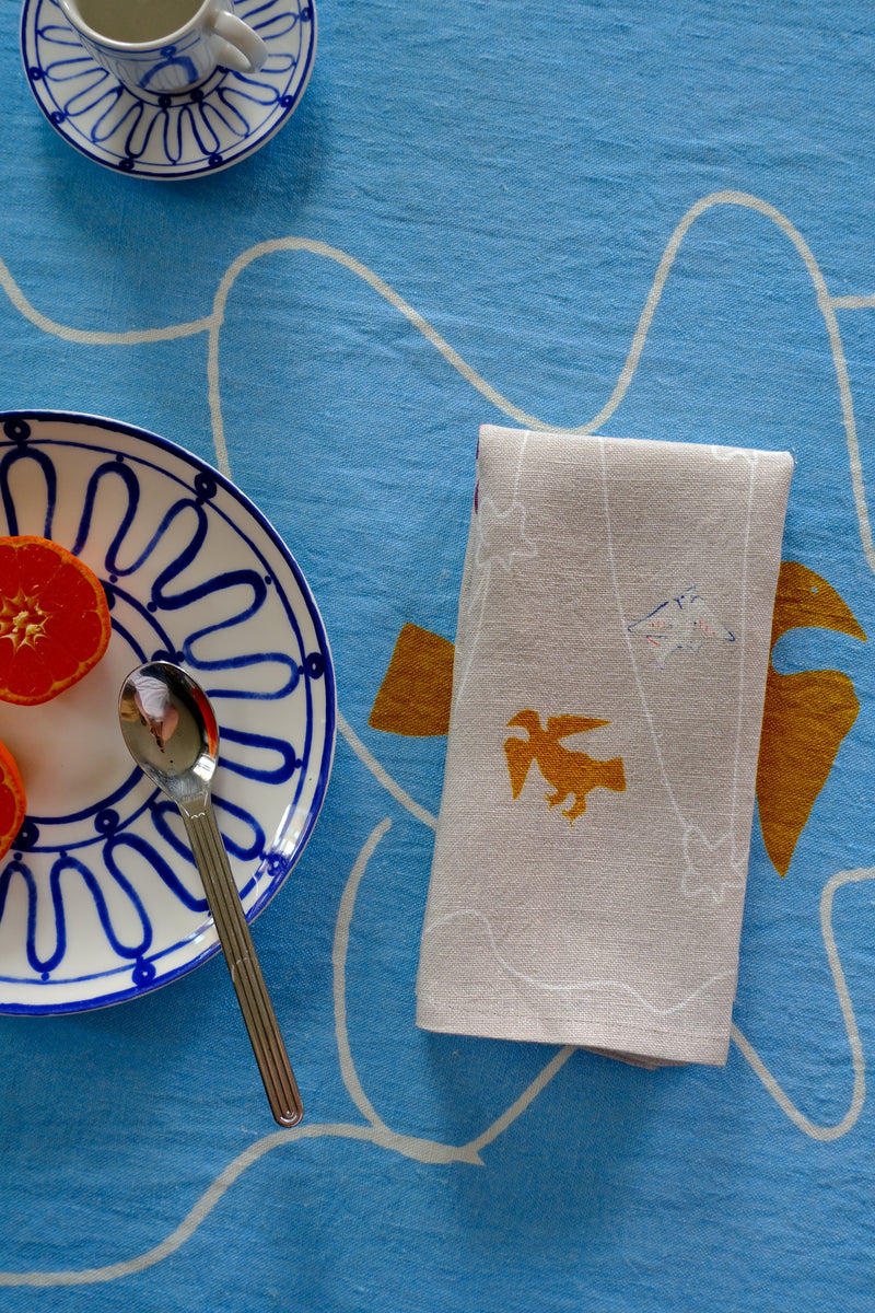Napkin with a fox design on a blue tablecloth with a plate and spoon.