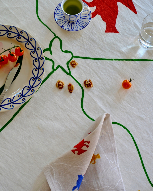 Table setting with a decorative tablecloth, plate with tomatoes, cup, and napkin.