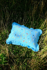 Blue pillow with embroidered designs on a grassy background