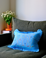 Blue embroidered pillow on an olive green couch with a vase of flowers in the background