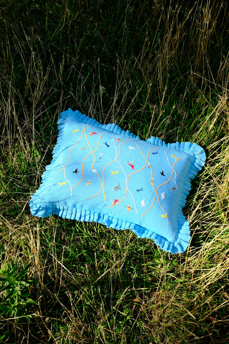 Blue pillow with embroidered designs on a grassy background