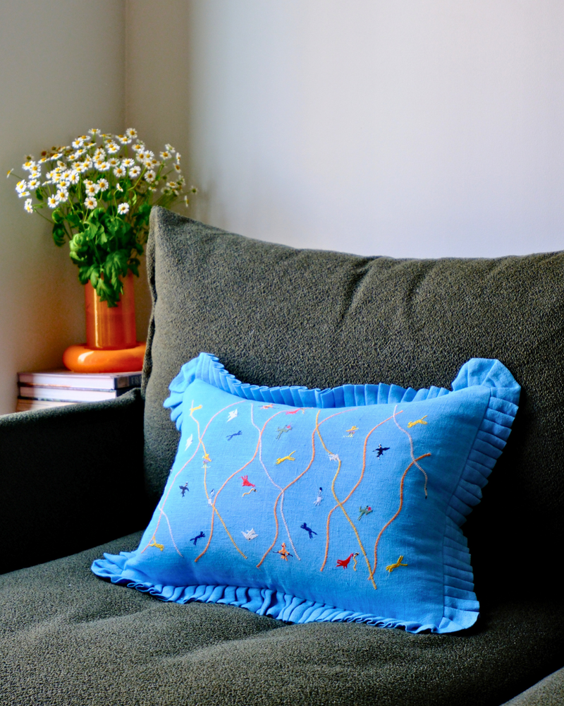 Blue embroidered pillow on an olive green couch with a vase of flowers in the background