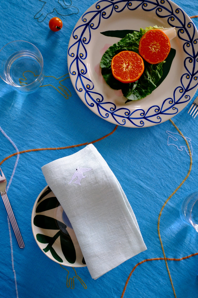 Dinner table setting with a decorative plate, white napkin, and cutlery on a blue tablecloth.