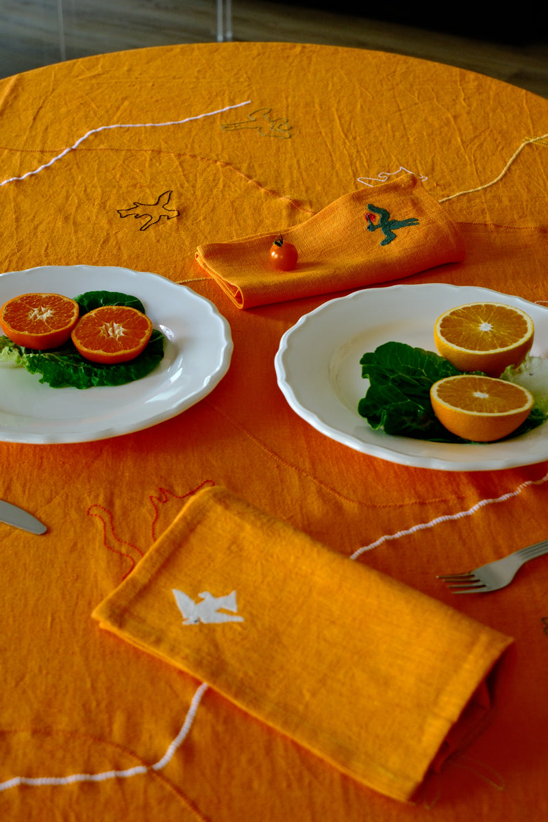 Orange tablecloth with two plates of food and a napkin on a table.