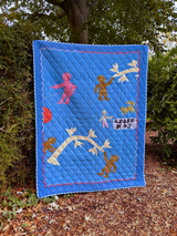 Asafo Blue quilt with colorful appliqué designs of children and animals, displayed outdoors.