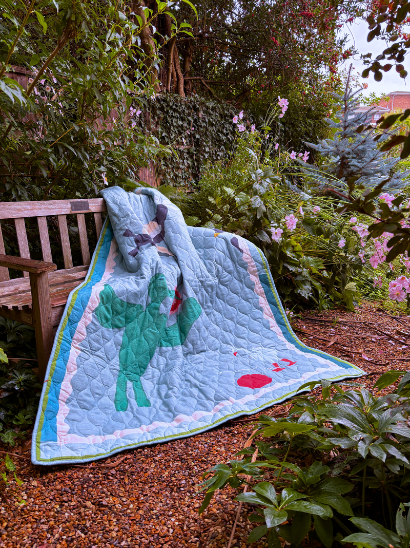 Asafo quilt with animal design on a wooden bench in a garden setting