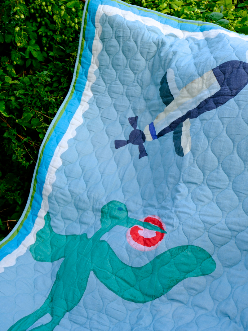 Quilt with a asafo design of a green creature holding a red heart, with a blue border.