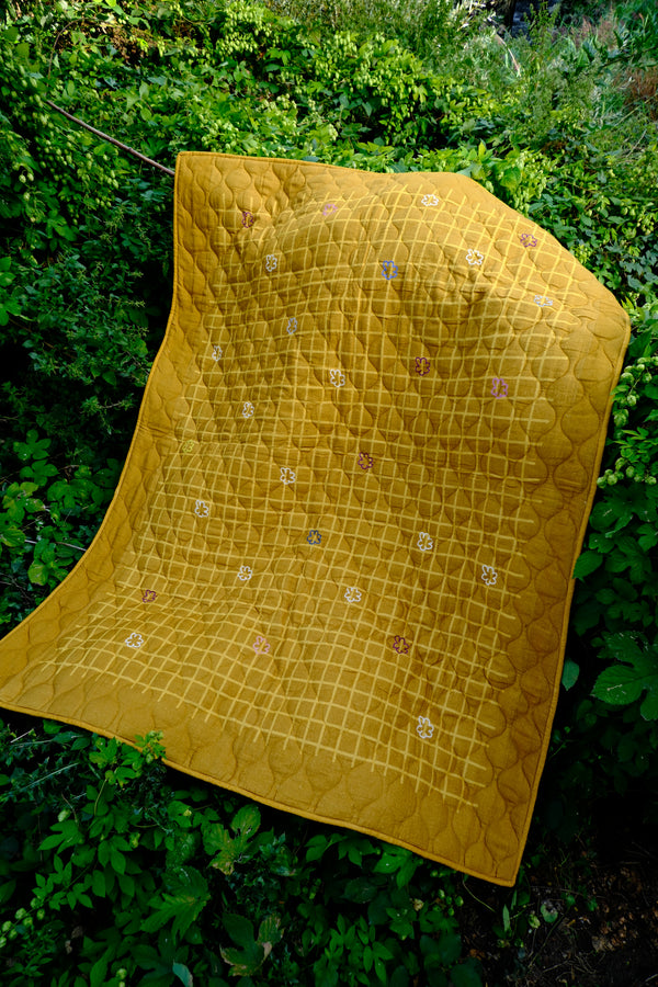 Orange quilt with a grid pattern on a green leafy background