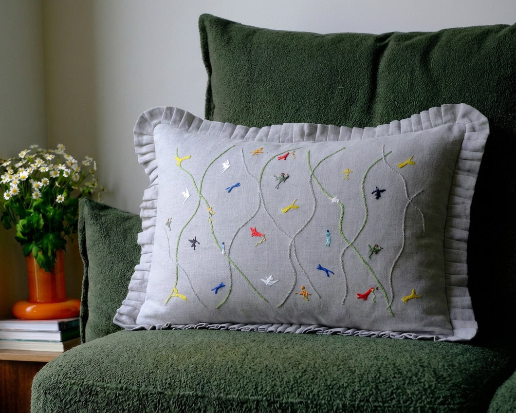 Grey embroidered cushion on a green couch with a plant and books in the background.