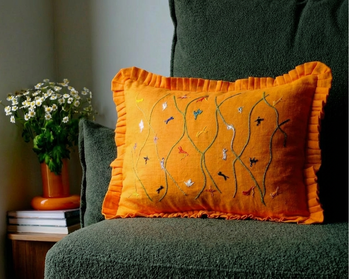 Orange cushion with embroidery on a green couch next to a plant